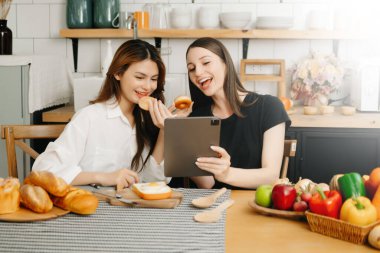 Mutfakta önlüklü iki güzel kadın, masaya taze sebzeler, en sevdiği tarifleri yazıyorlar, yemek için fikirler üretiyorlar. 