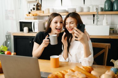 İki Asyalı öğrenci mutfaktaki akıllı telefondan ya da evdeki oturma odasından birlikte öğreniyor..