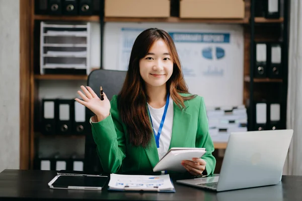 Confident Asian business expert attractive smiling young woman working on laptop at  desk in creative office