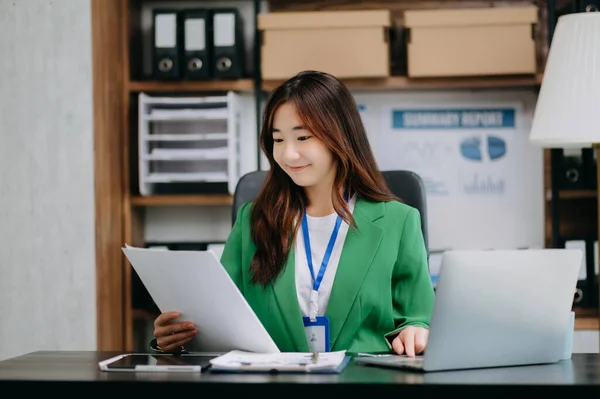 Confident Asian business expert attractive smiling young woman working on laptop at  desk in creative office
