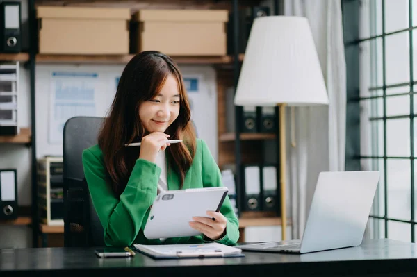 Confident Asian business expert attractive smiling young woman holding digital tablet  at desk in creative office