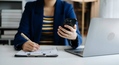İş kadını sabah vakti ofisteki masada akıllı telefon üzerinde çalışıyor.