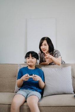 Anne izlerken oğlu kanepede oturup bilgisayar oyunu oynuyor. 