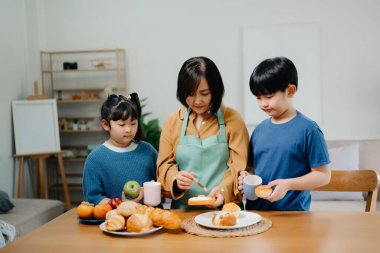 Asyalı bir aile mutfakta yemek yapıyor. Masanın yanında duran gülümseyen anne ve çocukların portresi..