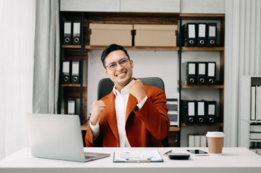 Asyalı iş adamı ofisteki dizüstü bilgisayardan memnun ve memnun..