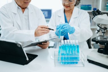 Bir tıp laboratuarında araştırma yapan kıdemli bilim adamları, ön plandaki bir araştırmacı tıp laboratuarında bir mikroskop kullanıyor.. 