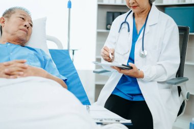 Doktor yaşlı erkek hastayla tedaviyi tartışıyor, modern klinikte ya da hastanede muayene odasında oturuyor.