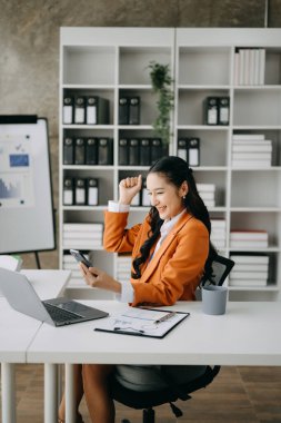 Ofiste çalışan mutlu Asyalı iş kadını akıllı telefon ve dizüstü bilgisayarla