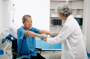 Asyalı fizyoterapist yaşlı bir adamın hastanede kolunu esnetmesine yardım ediyor.