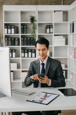 Genç işletme yöneticisi akıllı telefon kullanıyor, pazar araştırması yapıyor ve modern ofiste çalışıyor.