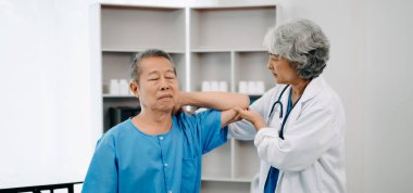 Asyalı fizyoterapist yaşlı bir adamın hastanede kolunu esnetmesine yardım ediyor.