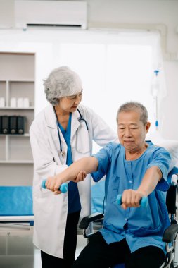 Asyalı fizyoterapist yaşlı bir adamın hastanede kolunu esnetmesine yardım ediyor.
