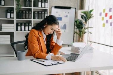 Asyalı kadın migren ağrısı çekiyor. Ofiste dizüstü bilgisayarla çalışan aşırı çalışan iş kadını finansör.