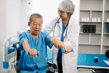 Asyalı fizyoterapist yaşlı bir adamın hastanede kolunu esnetmesine yardım ediyor.