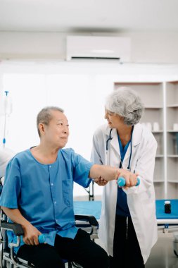 Asyalı fizyoterapist yaşlı bir adamın hastanede kolunu esnetmesine yardım ediyor.