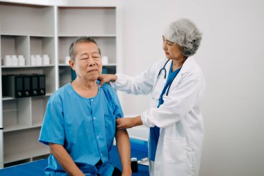 Asyalı fizyoterapist yaşlı bir adamın hastanede kolunu esnetmesine yardım ediyor.