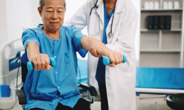 Asyalı fizyoterapist yaşlı bir adamın hastanede kolunu esnetmesine yardım ediyor.