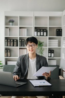 Genç işletme yöneticisi dizüstü bilgisayar kullanıyor, pazar araştırması yapıyor ve modern ofiste çalışıyor.