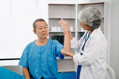 Asyalı fizyoterapist yaşlı bir adamın hastanede kolunu esnetmesine yardım ediyor.