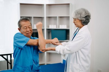 Asyalı fizyoterapist yaşlı bir adamın hastanede kolunu esnetmesine yardım ediyor.