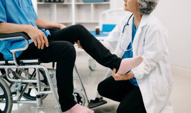 Asyalı fizyoterapist yaşlı adamın hastanede bacağını esnetmesine yardım ediyor.