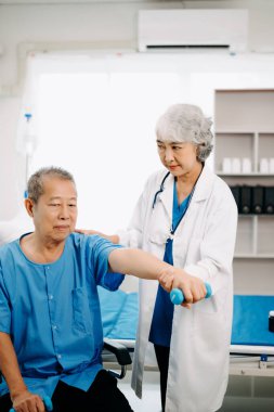 Asyalı fizyoterapist yaşlı bir adamın hastanede kolunu esnetmesine yardım ediyor.