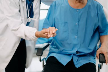 Asyalı fizyoterapist hastanede tekerlekli sandalyedeki yaşlı adama yardım ediyor.