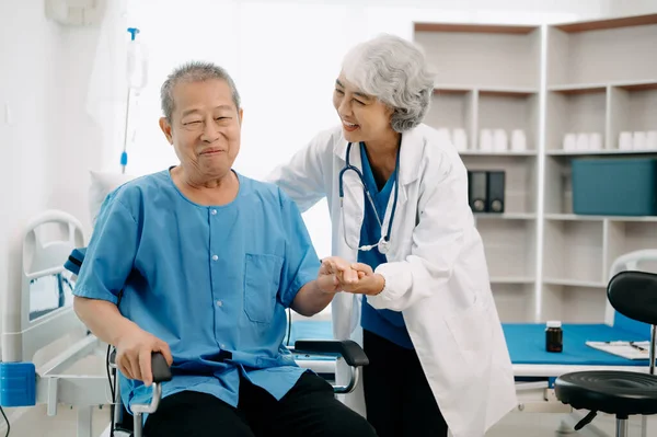 Asyalı fizyoterapist hastanede tekerlekli sandalyedeki yaşlı adama yardım ediyor.