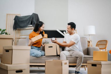 Büyük kutuları olan genç bir çift yeni bir eve taşınıyor. Asyalı erkek ve kadın yeni ev için kutu taşımaya yardım ediyorlar.