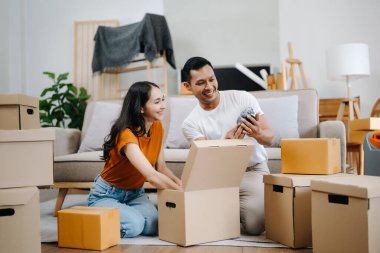 Happy asian young attractive couple man and woman with big boxes moving into a new house clipart