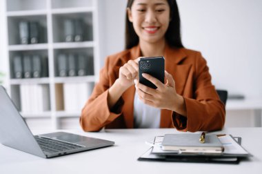 Çalışan beyaz masa ofisinde otururken akıllı telefon ve dizüstü bilgisayar kullanan güzel bir kadın.