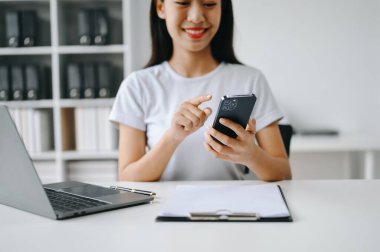 Cep telefonu kullanan bir kadın online alışveriş yapıyor, masada oturuyor.