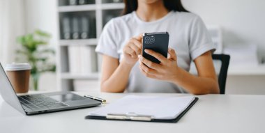 Cep telefonu kullanan bir kadın online alışveriş yapıyor, masada oturuyor.