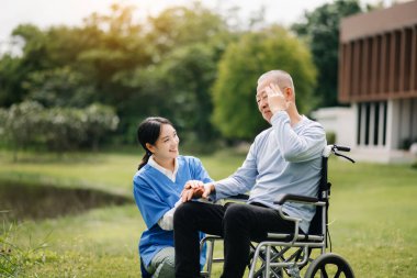 Asyalı yaşlı, yaşlı, tekerlekli sandalyede, Asyalı, dikkatli bir bakıcı. Hastane bahçesinde hemşire.