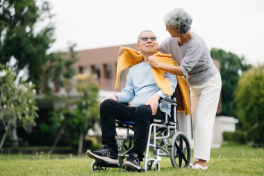 Tekerlekli sandalyede oturan Asyalı yaşlı adam, birbirine bakan kadın, romantik zaman. Parkta gülüp gülüyorlar.