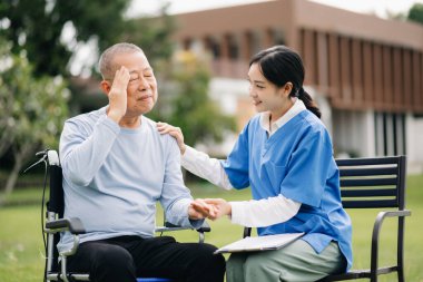 Asyalı yaşlı, yaşlı, tekerlekli sandalyede, Asyalı, dikkatli bir bakıcı ve bahçede hastaları teşvik eden bir adam.. 
