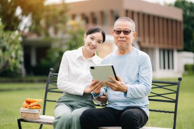 Mutlu yetişkin torun ve büyükbaba parkta dijital tablet kullanıyor.