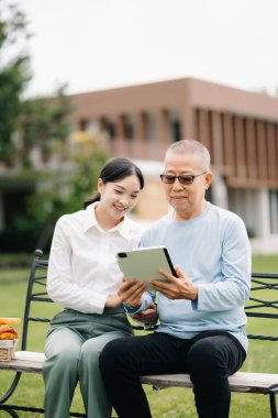 Mutlu yetişkin torun ve büyükbaba parkta dijital tablet kullanıyor.