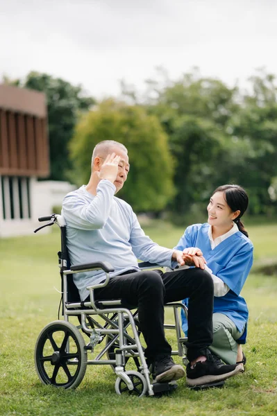 Elderly asian senior man on wheelchair with Asian careful caregiver. Nursing in hospital garden