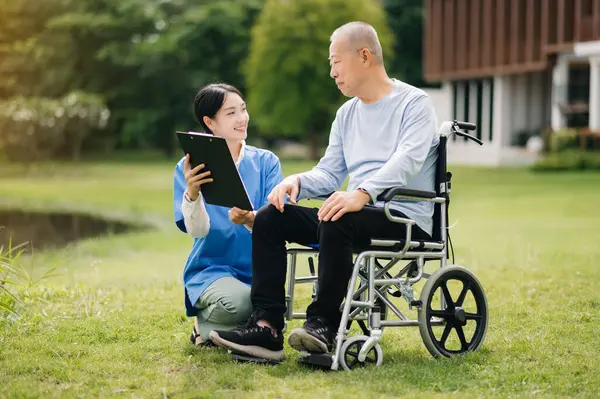 Elderly asian senior man on wheelchair with Asian careful caregiver and encourage patient in garden.