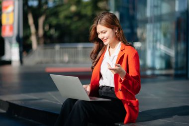 Girişimci şehir caddesinde otururken dizüstü bilgisayar, tablet üzerinde çalışıyor. Güzel, iş kadını dizüstü bilgisayar çantası taşıyor ve şehir dışında iş yapıyor.