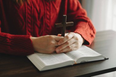 Oturan ve kutsal kitabı okuyan kadın. Ellerindeki tahta haç. Hıristiyan eğitimi kutsal yazıtların açılıp Tanrı 'ya dua etmesini sağlar.