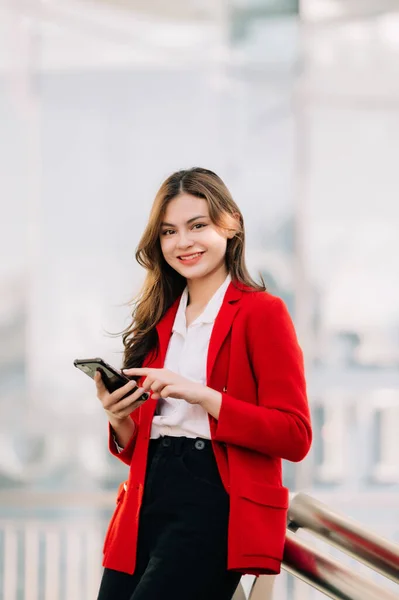 Business expert attractive smiling young woman holding smartphone on street in city Outside Office