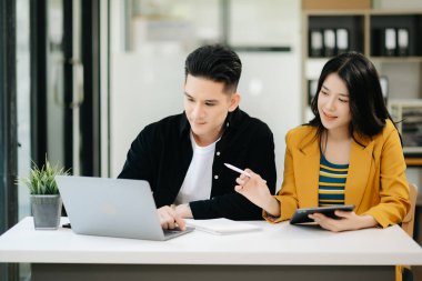 Asyalı işadamı sunar ve meslektaşına dizüstü bilgisayar kullanarak yeni projeyi açıklar. Takım çalışması, finansal pazarlama ekibi, modern ofis odasında otururken.