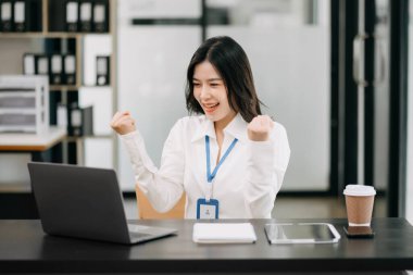 Ofiste dizüstü bilgisayarla çalışan Asyalı mutlu bir iş kadını.