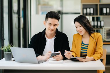 Asyalı işadamı sunar ve meslektaşına dizüstü bilgisayar kullanarak yeni projeyi açıklar. Takım çalışması, finansal pazarlama ekibi, modern ofis odasında otururken.
