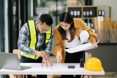 Mühendis takımı buluşması, birlikte çalışmak, mimari proje sahasında işçi yelekleri giymek ve model ev yapmak. Modern ofiste Asya endüstrisi profesyonel takımı