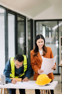 Mühendis takımı buluşması, birlikte çalışmak, mimari proje sahasında işçi yelekleri giymek ve model ev yapmak. Modern ofiste Asya endüstrisi profesyonel takımı
