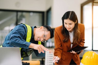 Mühendis takımı buluşması, birlikte çalışmak, mimari proje sahasında işçi yelekleri giymek ve model ev yapmak. Modern ofiste Asya endüstrisi profesyonel takımı