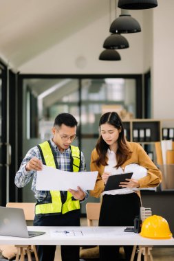 Mühendis takımı buluşması, birlikte çalışmak, mimari proje sahasında işçi yelekleri giymek ve model ev yapmak. Modern ofiste Asya endüstrisi profesyonel takımı